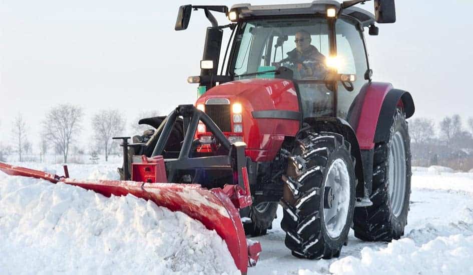 En medarbejder fra Roskilde Ejendomsservice rydder sne ved brug af en rød traktor.